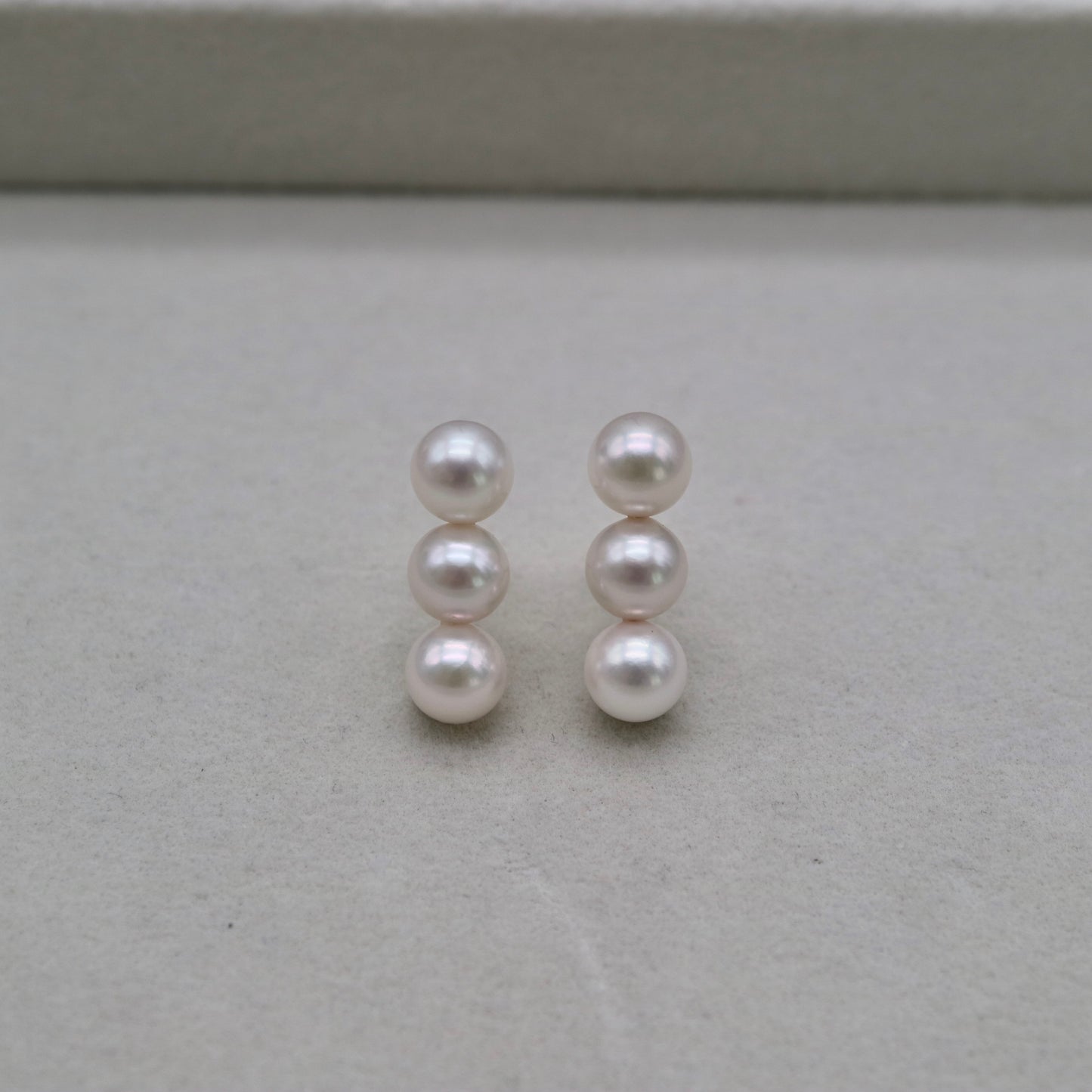 Handmade Japanese Akoya pearl earrings with three lustrous pearls each, displayed on neutral background