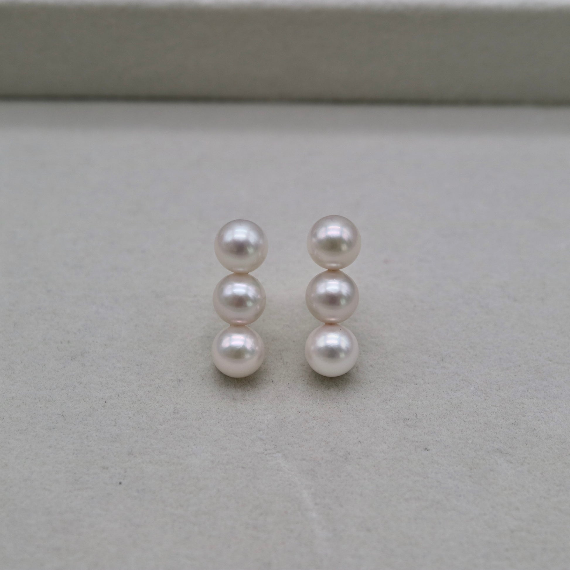 Handmade Japanese Akoya pearl earrings with three lustrous pearls each, displayed on neutral background
