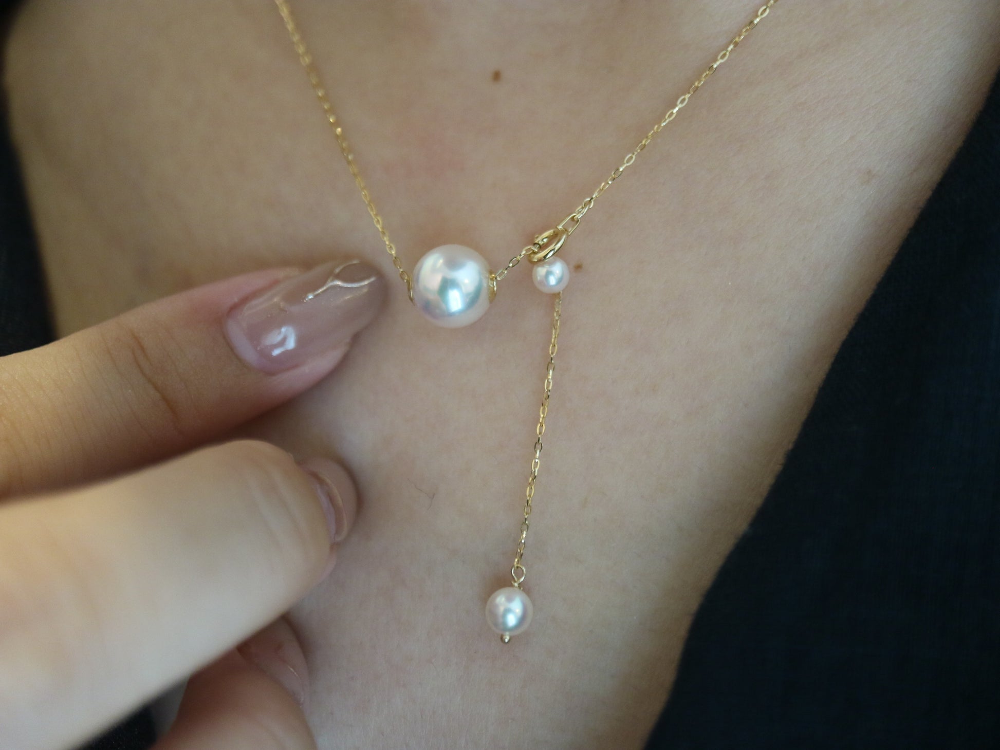 Close-up of a delicate gold necklace with three white pearls worn on skin with polished nails