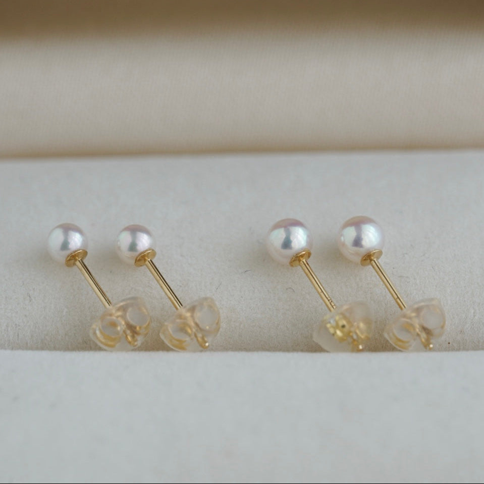 Handmade Japanese Akoya pearl stud earrings with gold posts, displayed on soft fabric