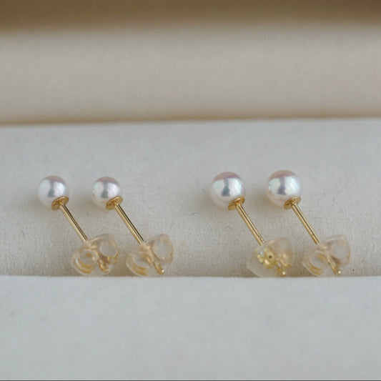 Handmade Japanese Akoya pearl stud earrings with gold posts, displayed on soft fabric