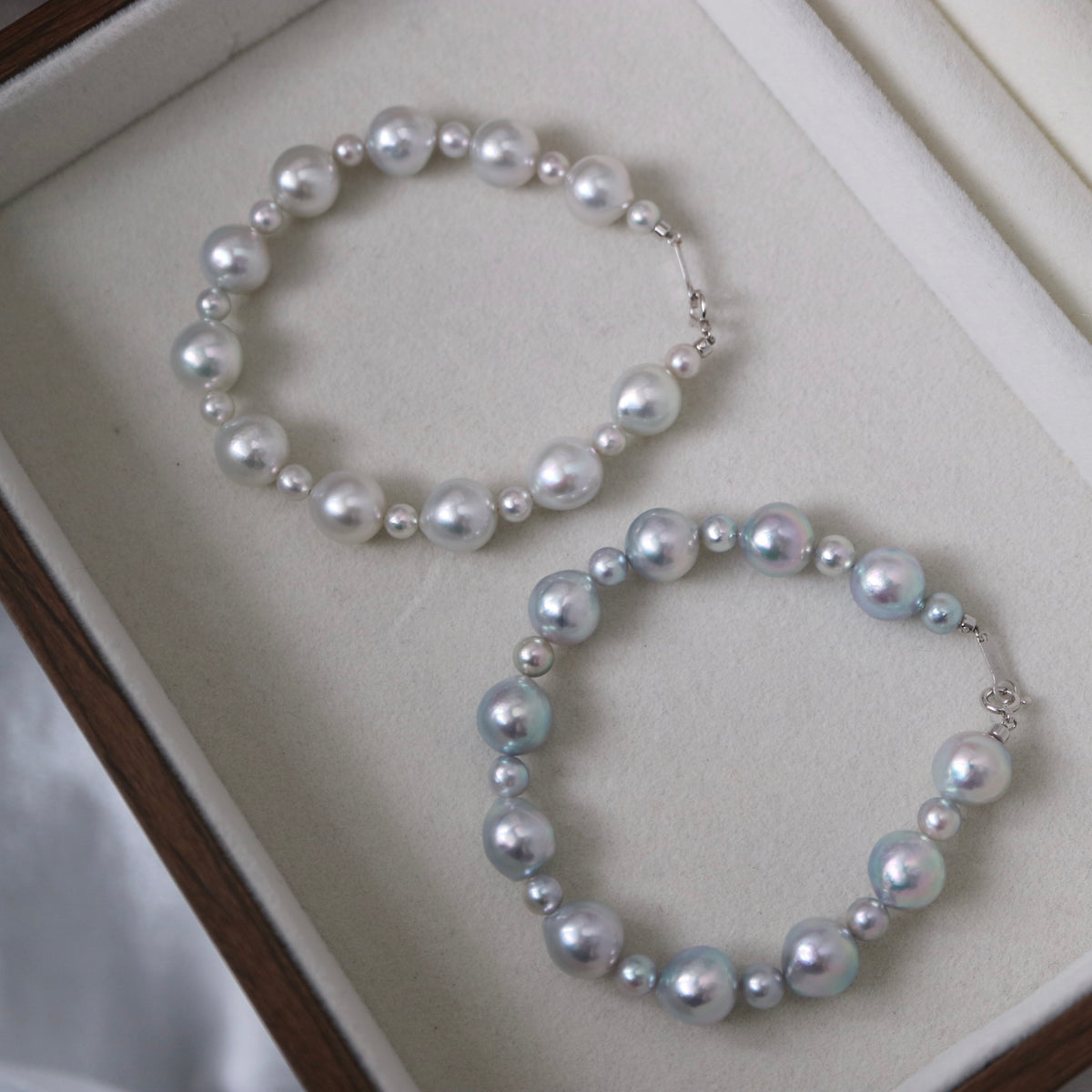 Two elegant pearl necklaces with lustrous Akoya pearls in white and blue hues, displayed in a jewelry box.