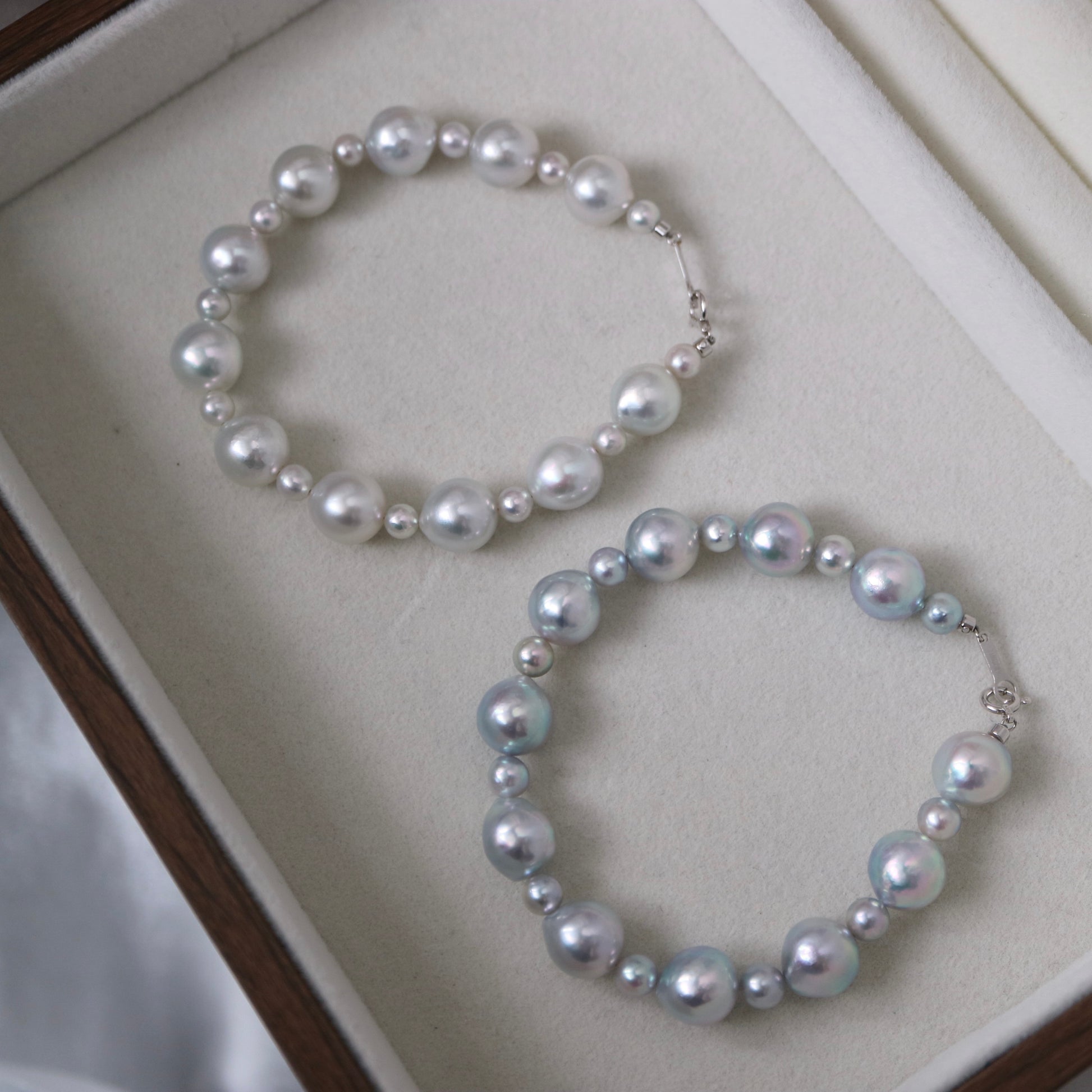 Two elegant pearl necklaces with lustrous Akoya pearls in white and blue hues, displayed in a jewelry box.