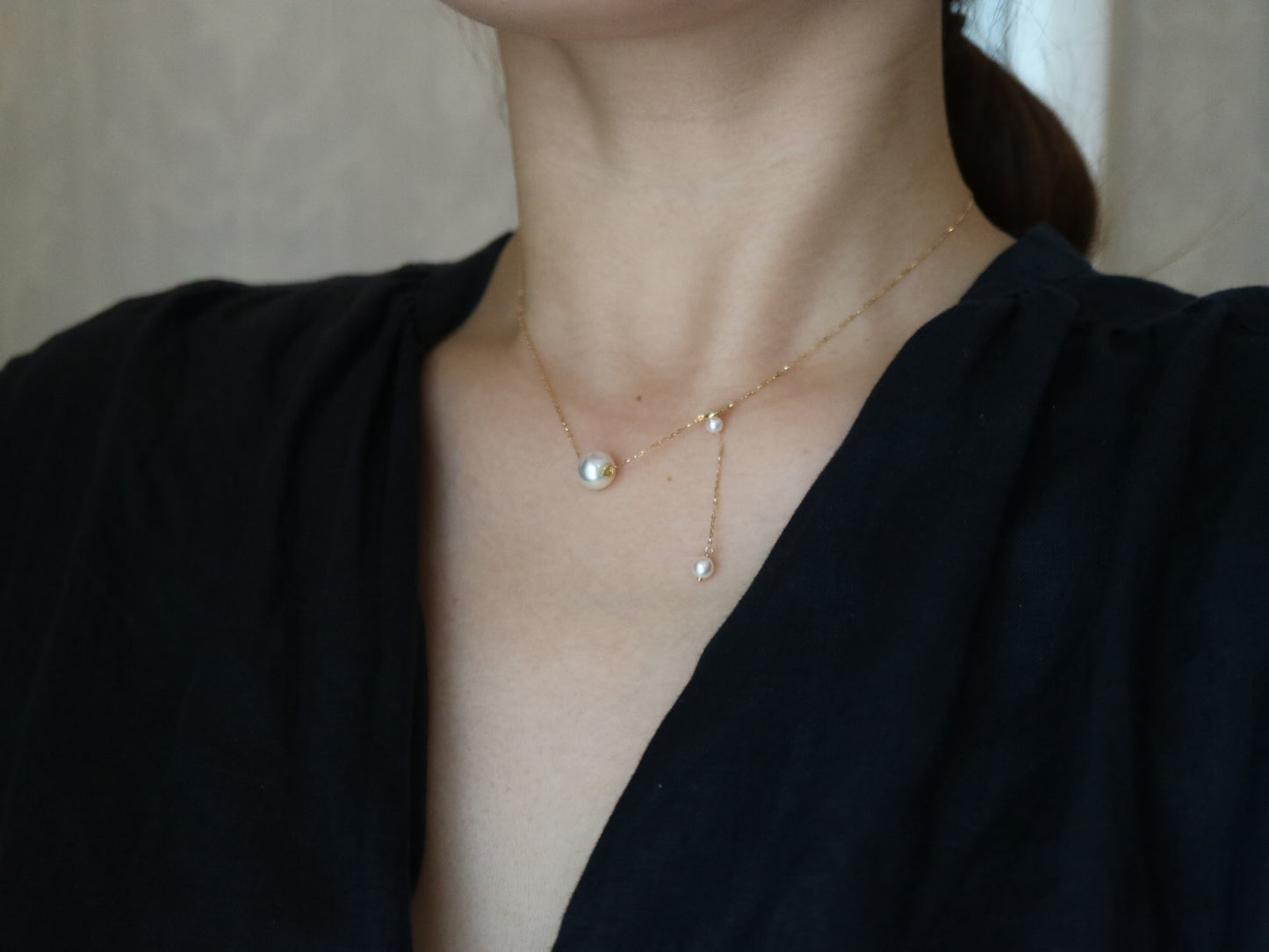 Close-up of woman wearing elegant gold chain necklace with three pearls and black top