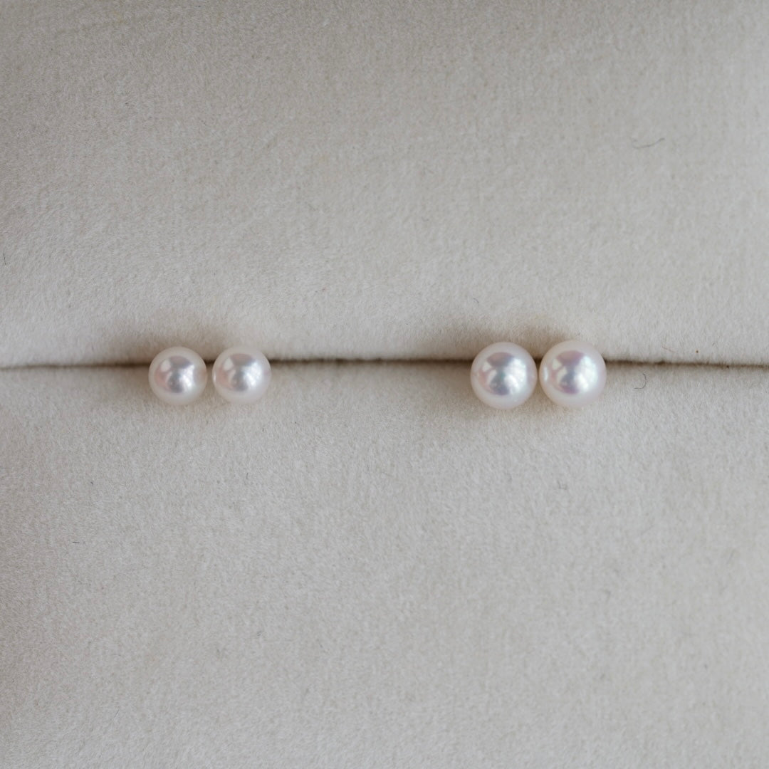 Handmade Japanese Akoya pearl earrings, lustrous and elegant, displayed on soft beige fabric.