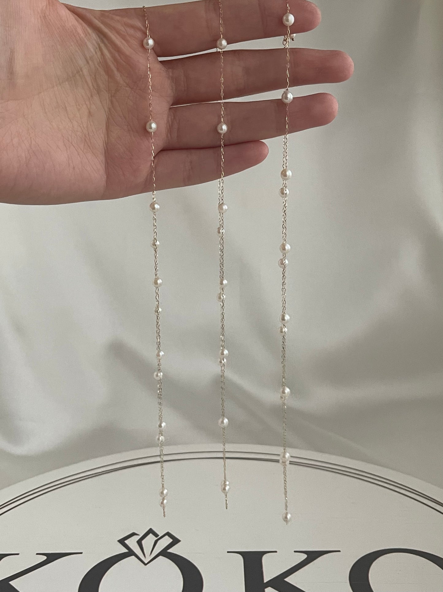手持精緻的日本 Akoya 珍珠垂墜耳環，搭配金色鏈條，展現手工優雅。