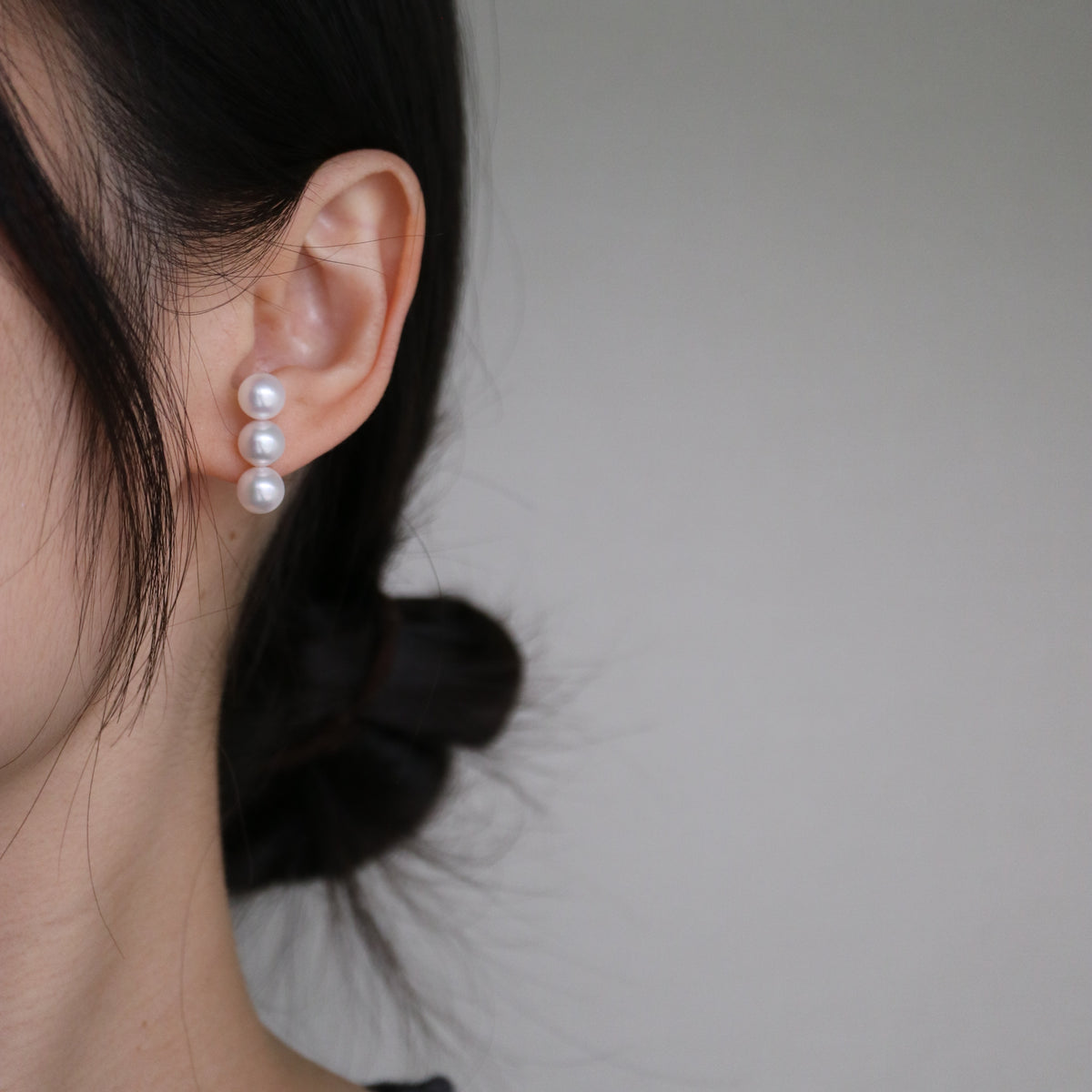 Elegant triple Akoya pearl drop earrings worn on ear, showcasing lustrous seawater pearls for timeless jewelry style