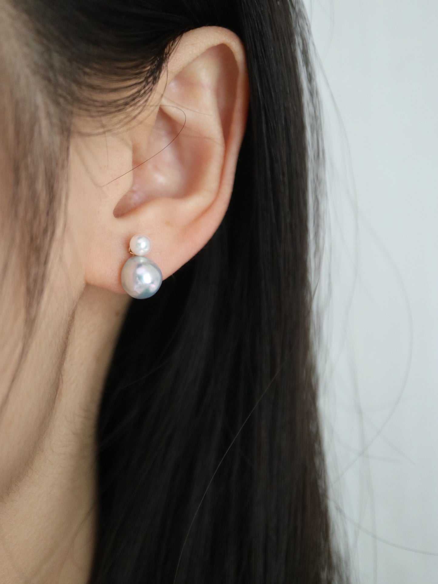 Close-up of a person wearing double-layered Akoya pearl stud earrings.