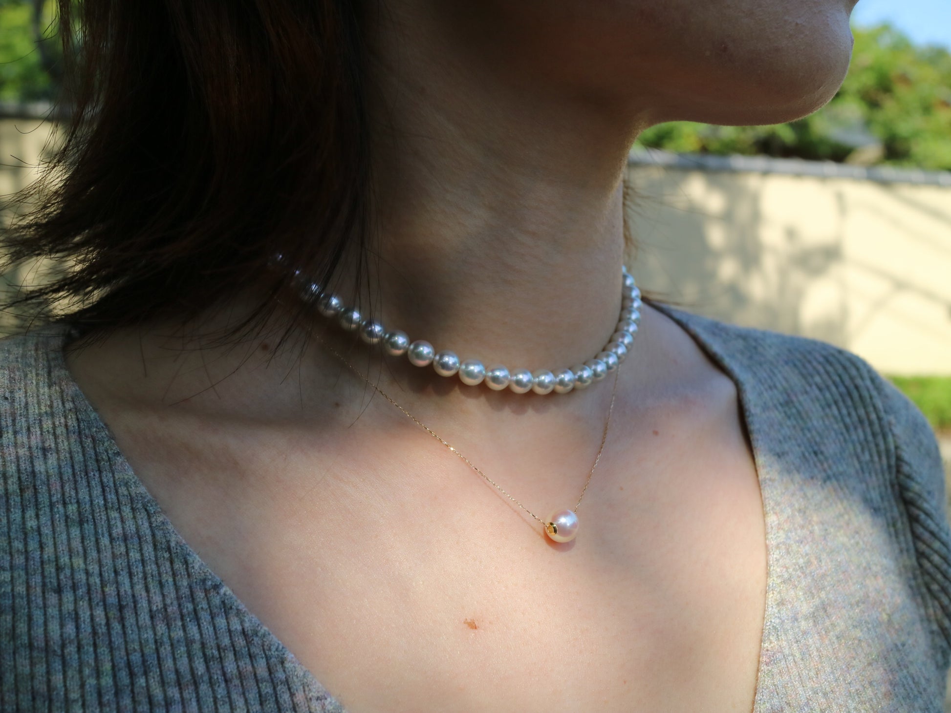 Close-up of a woman wearing a pearl choker and a delicate gold chain necklace with a single pearl pendant