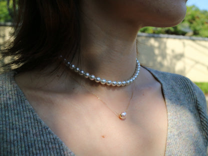 Close-up of a woman wearing a pearl choker and a delicate gold chain necklace with a single pearl pendant