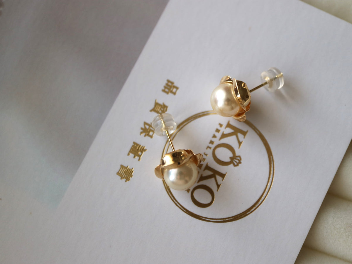 Pair of Akoya pearl stud earrings with gold settings on a white display card.