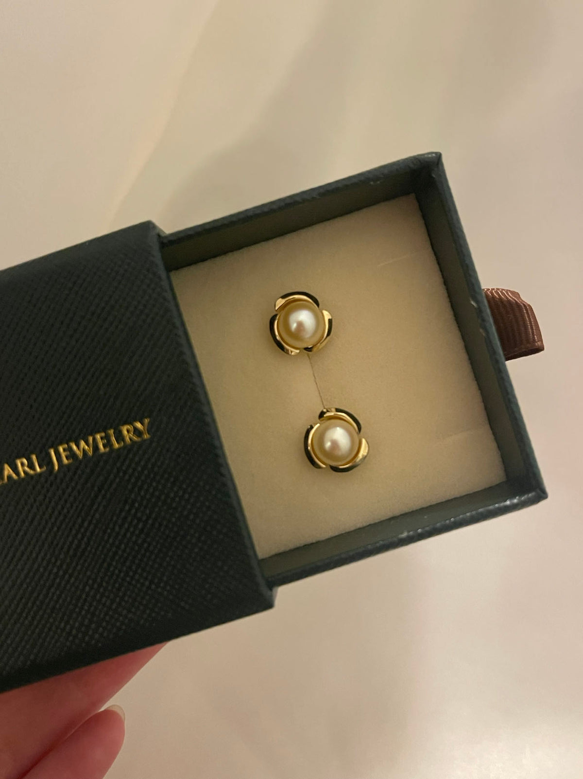 Pair of gold Akoya pearl stud earrings in a dark green jewelry box