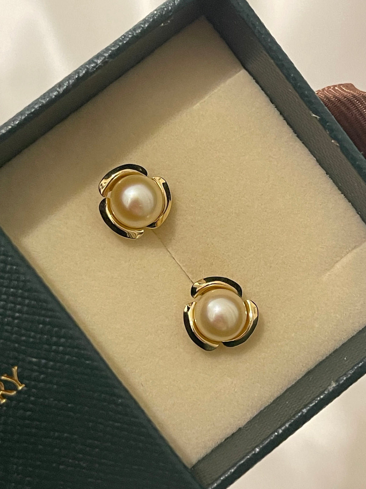 Pair of Japanese Akoya pearl stud earrings in gold settings inside a dark green jewelry box