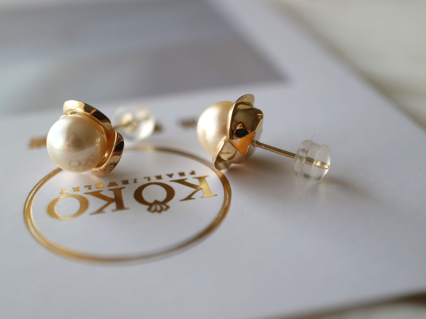 Pair of handmade Japanese Akoya pearl stud earrings with gold settings on a white card.