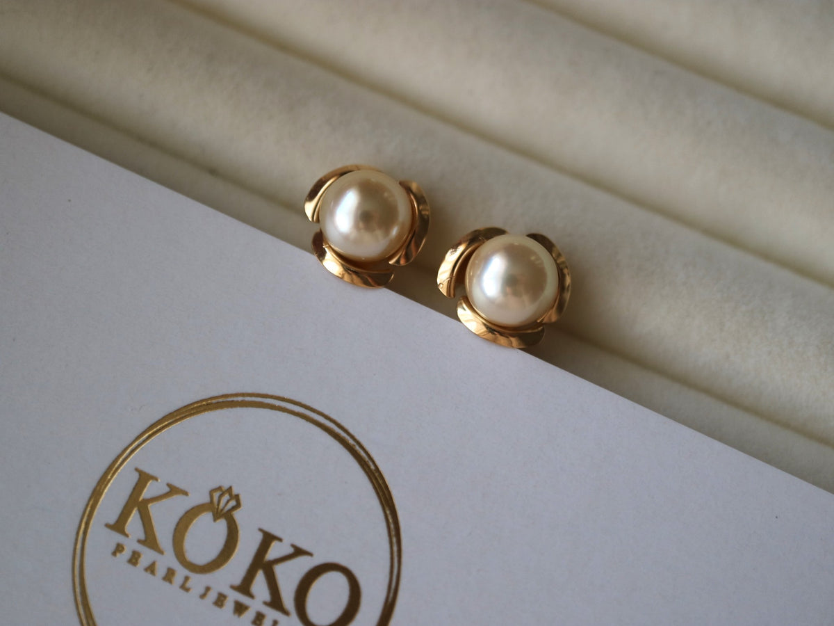 Pair of Akoya pearl stud earrings with gold floral settings on a white jewelry box