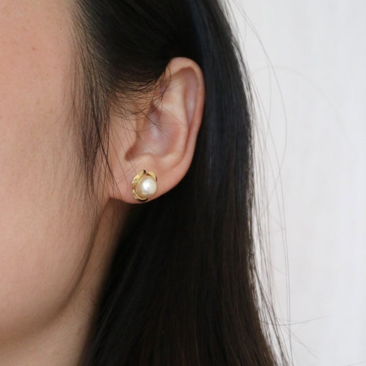 Close-up of a single Akoya pearl stud earring in a gold setting worn on an ear.