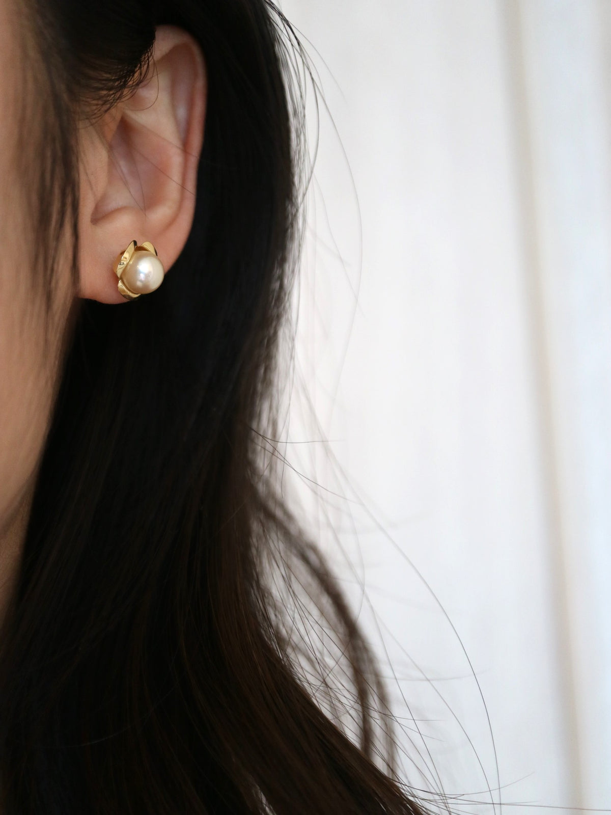 Close-up of a woman wearing a gold Akoya pearl stud earring.