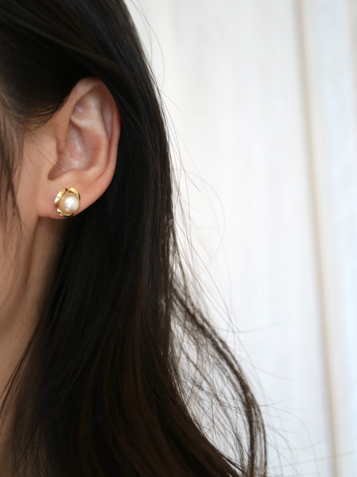 Close-up of a woman wearing a gold stud earring with a white Akoya pearl.