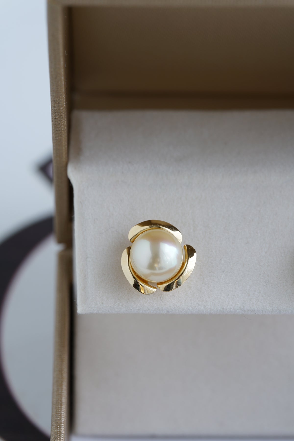Single gold stud earring with a white Akoya pearl in a jewelry box