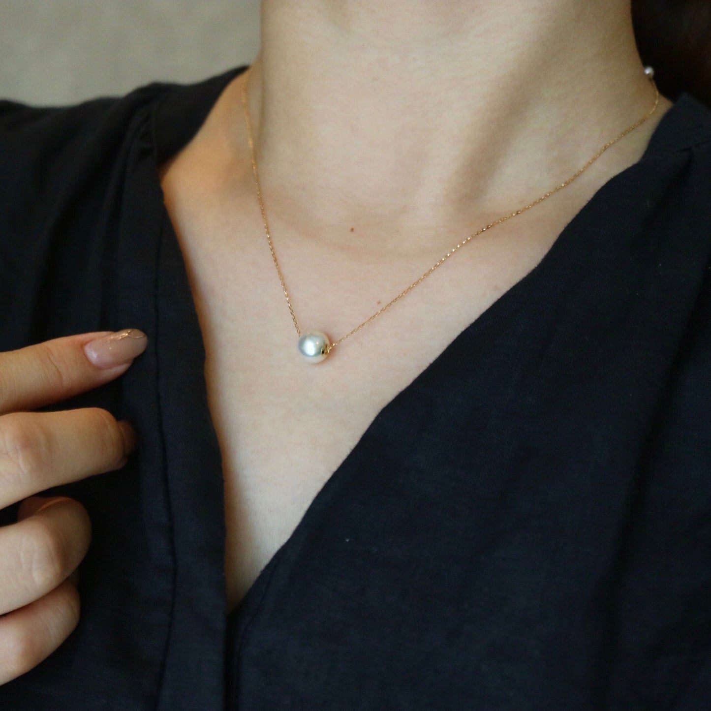 穿着黑色衣服的女性特写，佩戴精致金链单颗珍珠吊坠项链