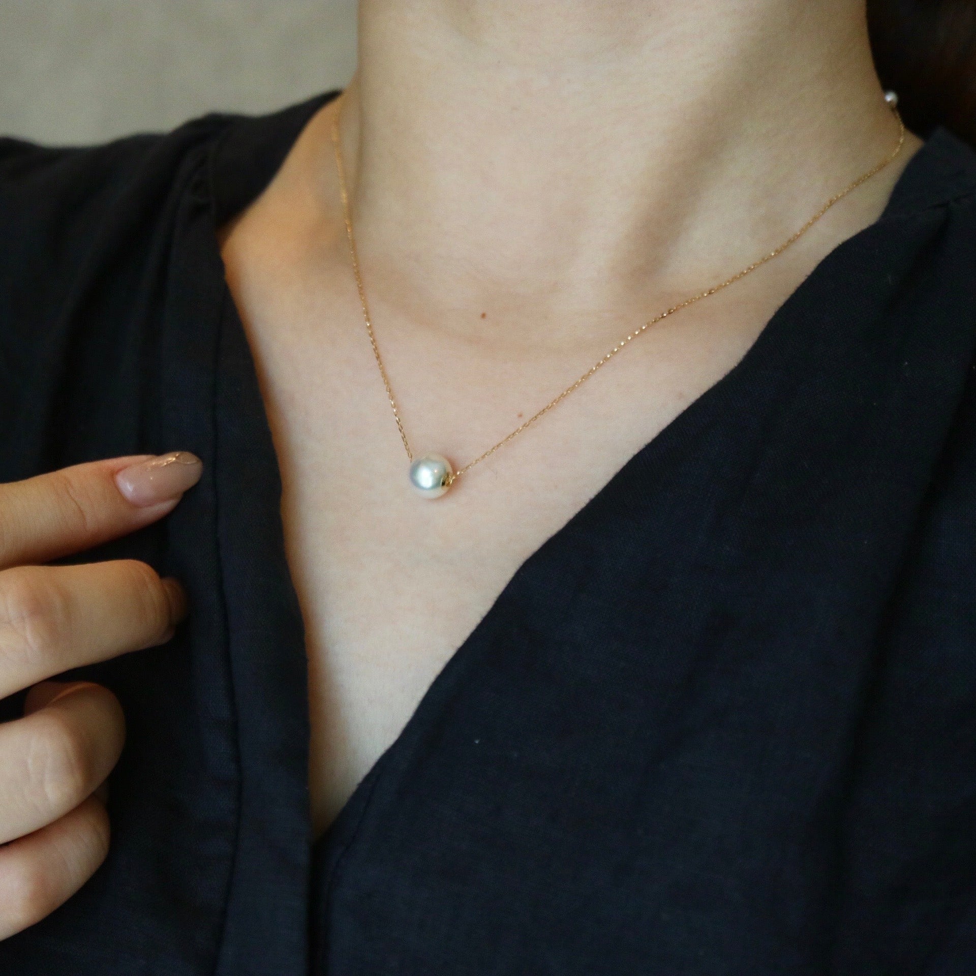 穿着黑色衣服的女性特写，佩戴精致金链单颗珍珠吊坠项链