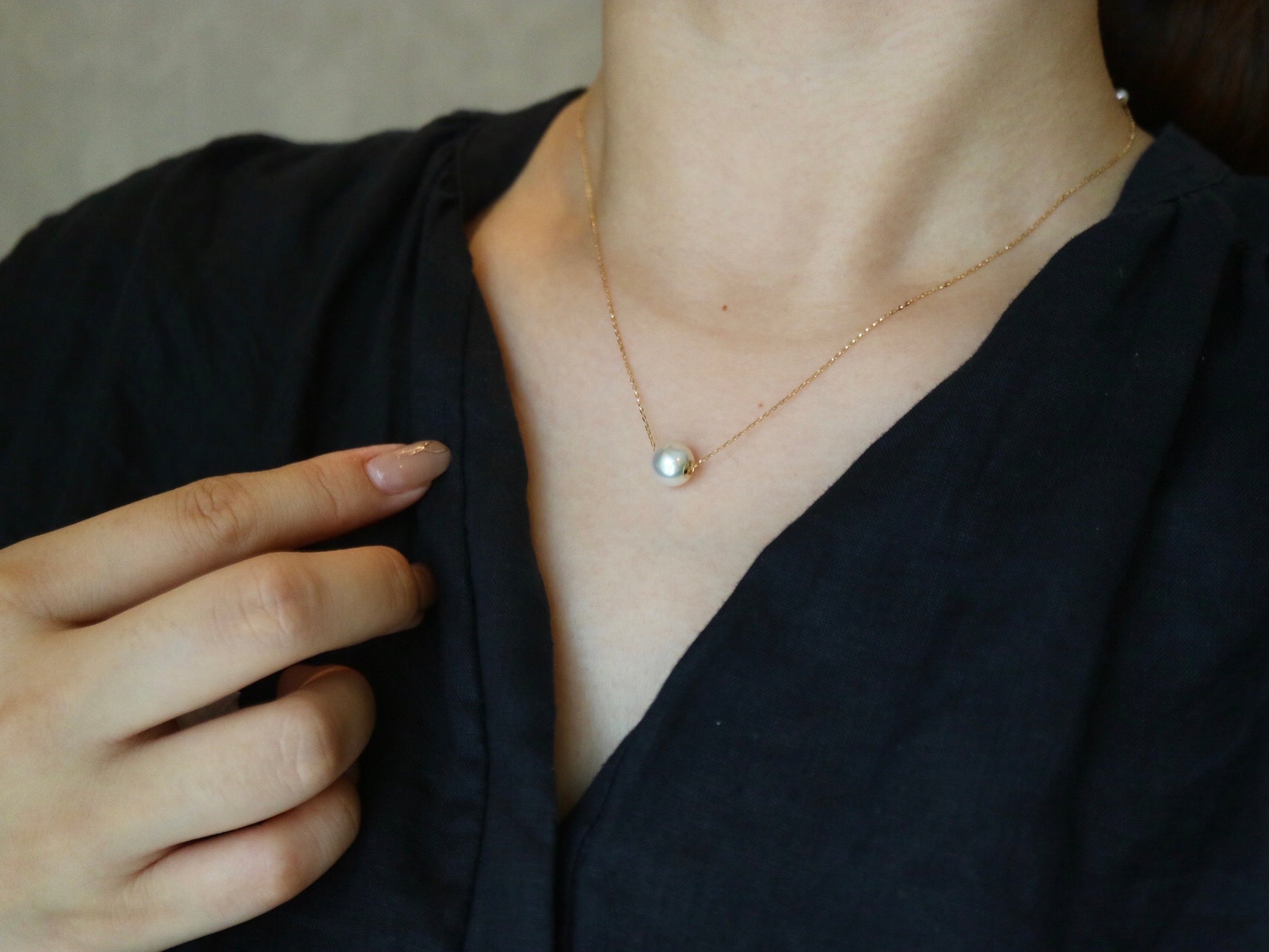 Close-up of woman wearing a delicate gold chain necklace with a single pearl pendant and black clothing
