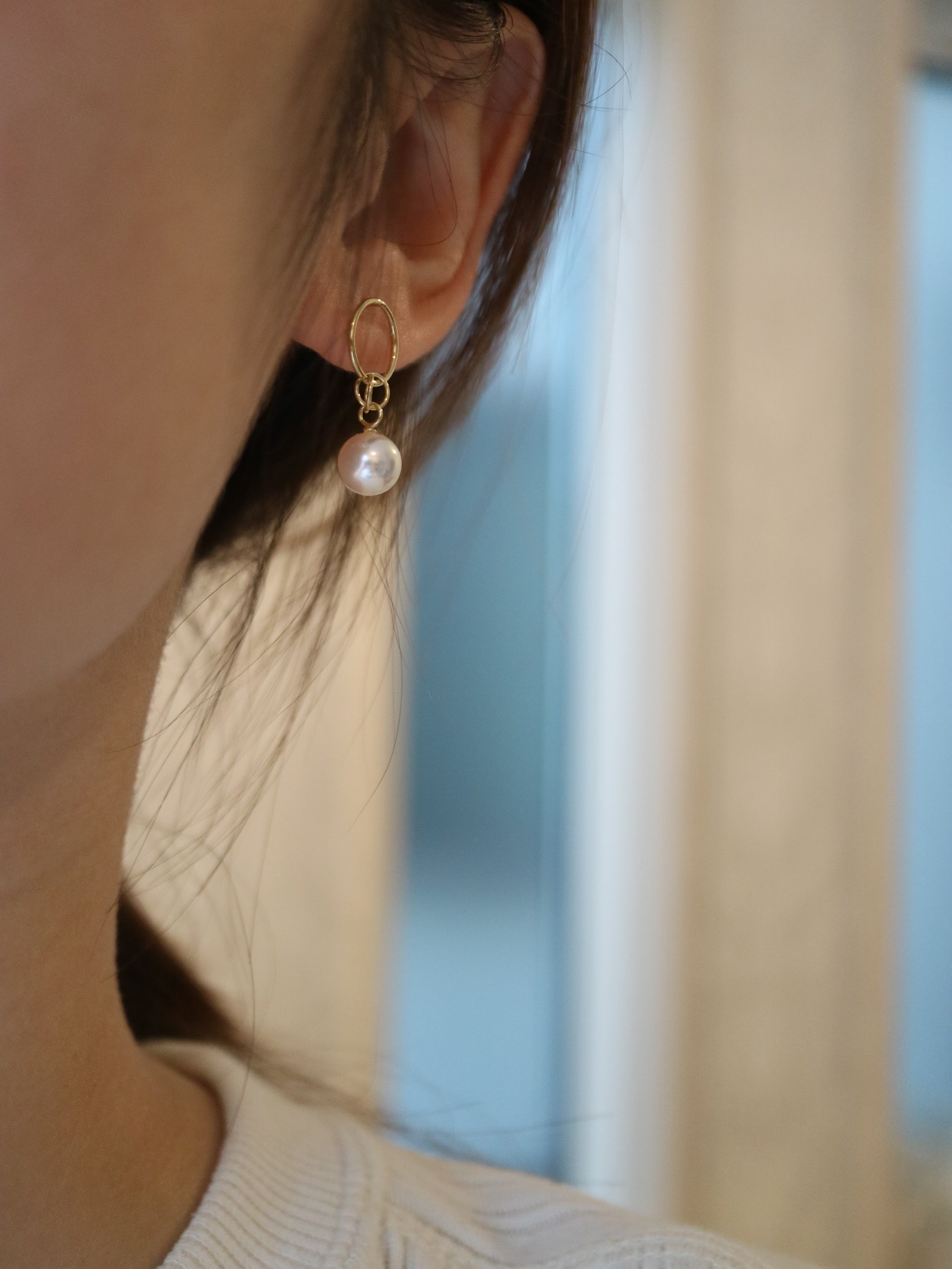 Close-up of a woman wearing a gold hoop earring with a single white Akoya pearl drop.
