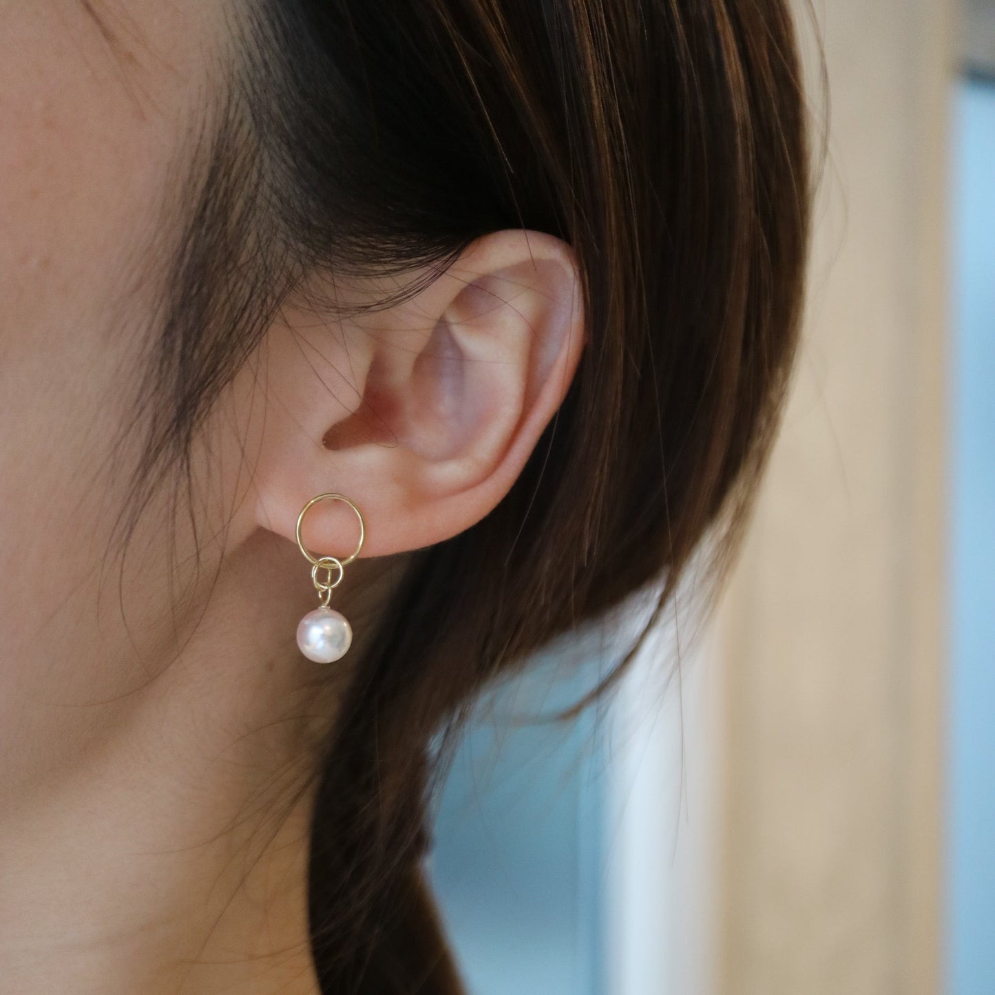 Close-up of a woman wearing a gold hoop earring with a single white Akoya pearl drop.