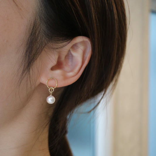 Close-up of a woman wearing a gold hoop earring with a single white Akoya pearl drop.