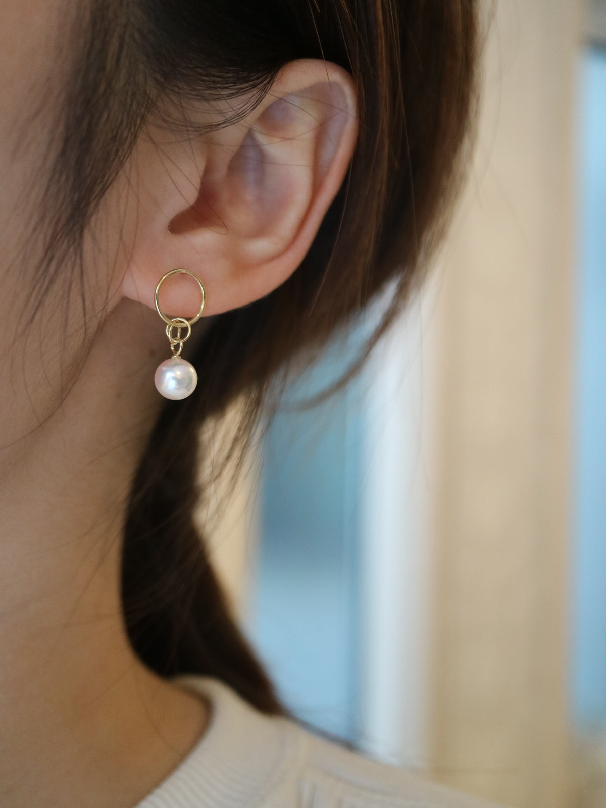 Close-up of a woman wearing a single gold hoop earring with a white Akoya pearl drop.