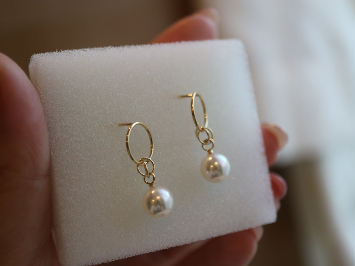 Handmade Japanese Akoya pearl drop earrings with gold hoops on a white jewelry display.