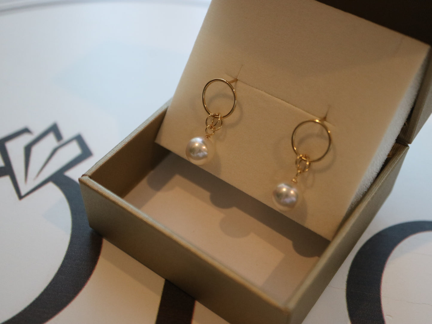 Gold hoop earrings with dangling Akoya pearls in a jewelry gift box