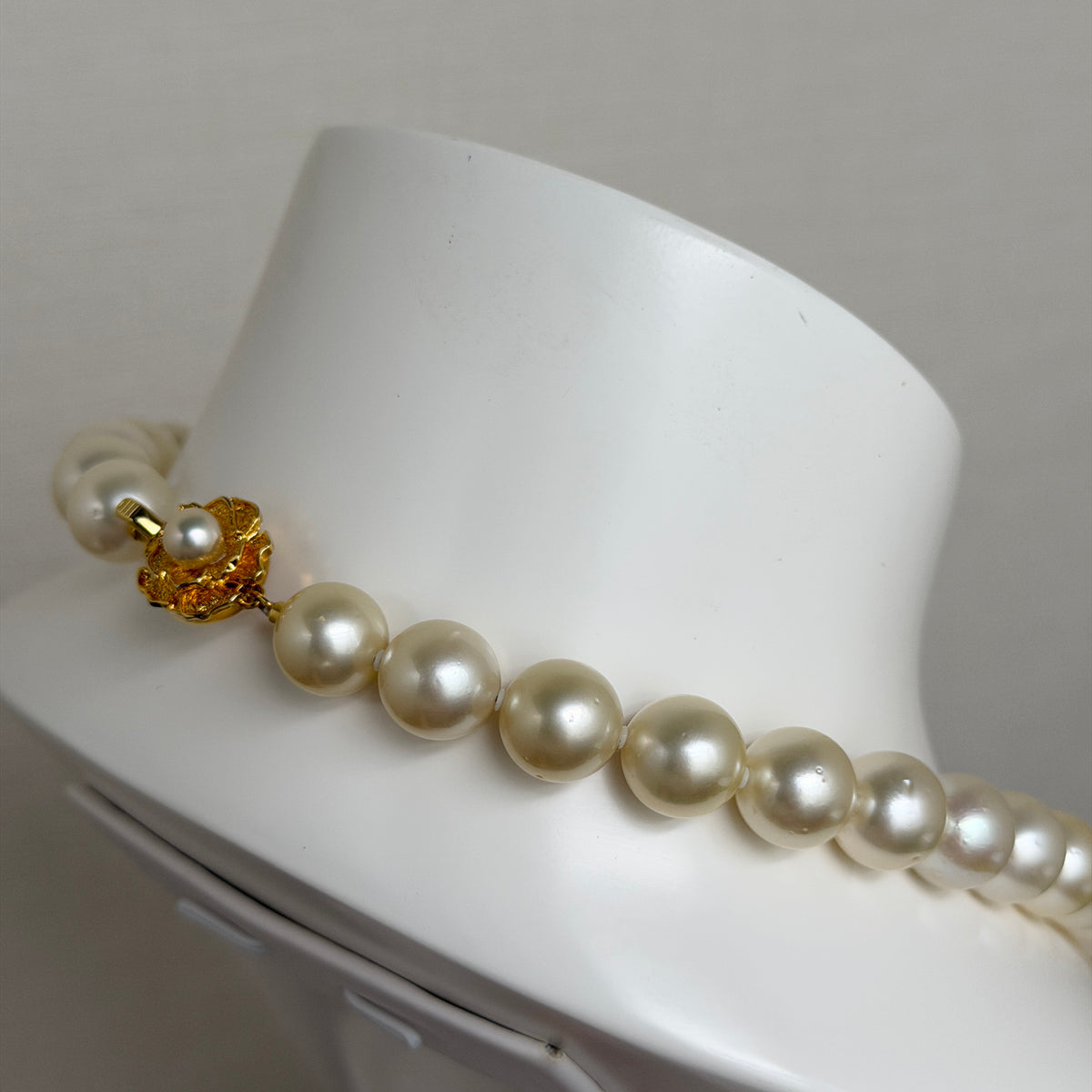 優雅的 Akoya 珍珠項鍊，配金色花朵扣環，展現光澤珍珠，置於白色展示底座上。