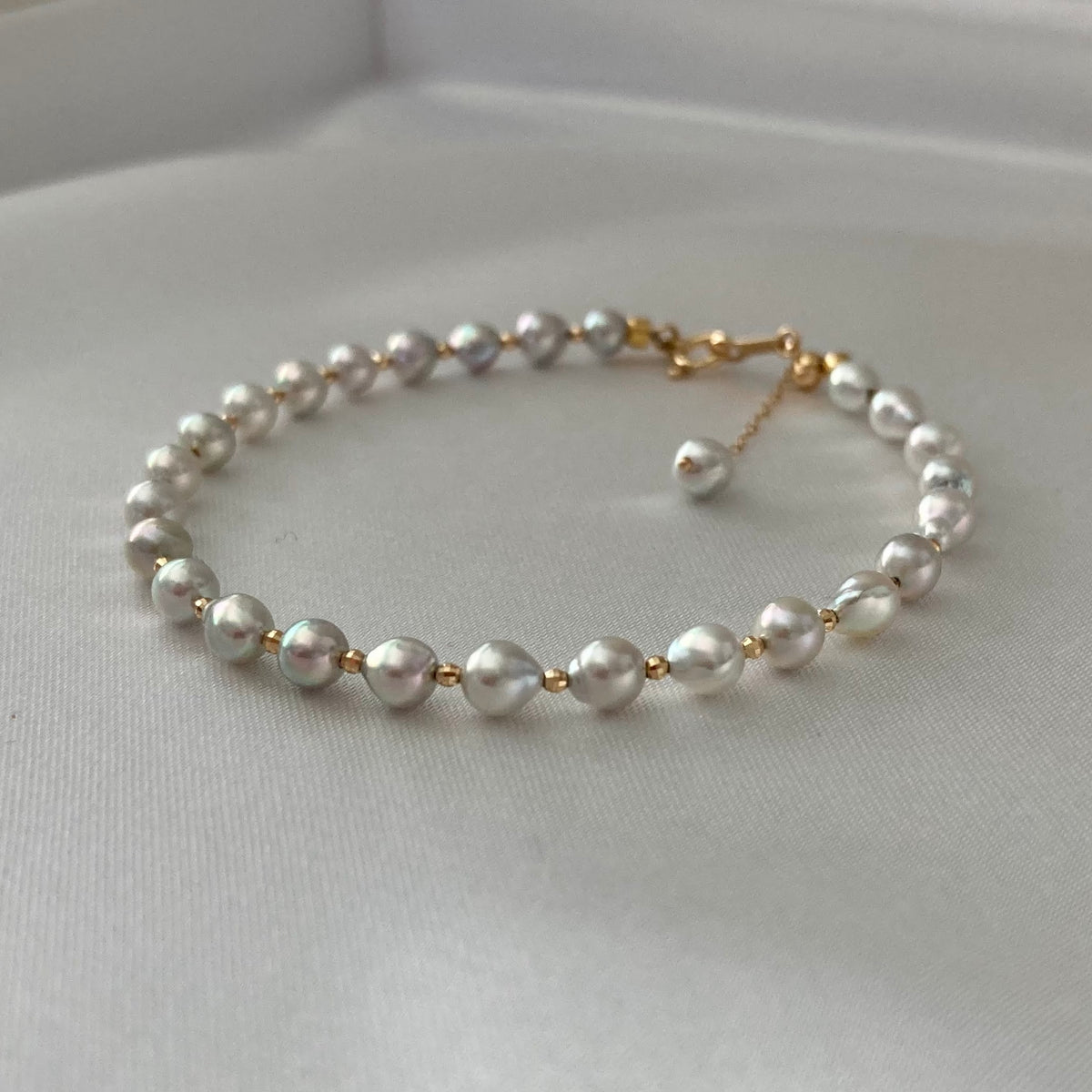 Elegantなアコヤ真珠のブレスレット。ゴールドのアクセントが上品で、やわらかな布の上に艶やかな海水真珠を美しく映す。