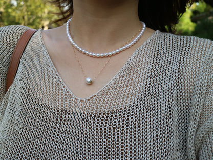Close-up of woman wearing pearl choker and single pearl pendant necklace with beige mesh top outdoors