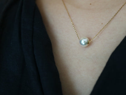 Close-up of a single white pearl pendant on a delicate gold chain necklace worn on bare skin with a black garment
