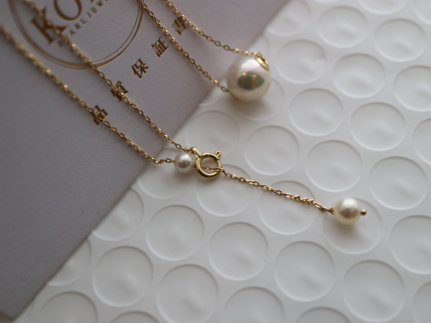 Close-up of delicate gold chain necklace with three pearls on textured white surface and gray card