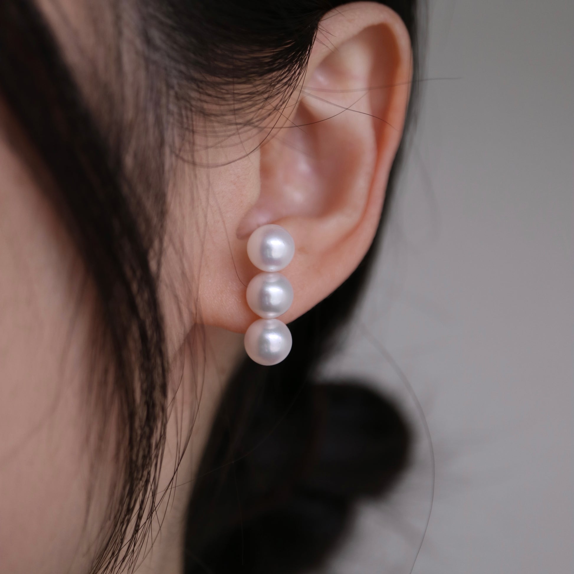 Elegant triple Akoya pearl drop earrings, showcasing lustrous seawater pearls on a model's ear.