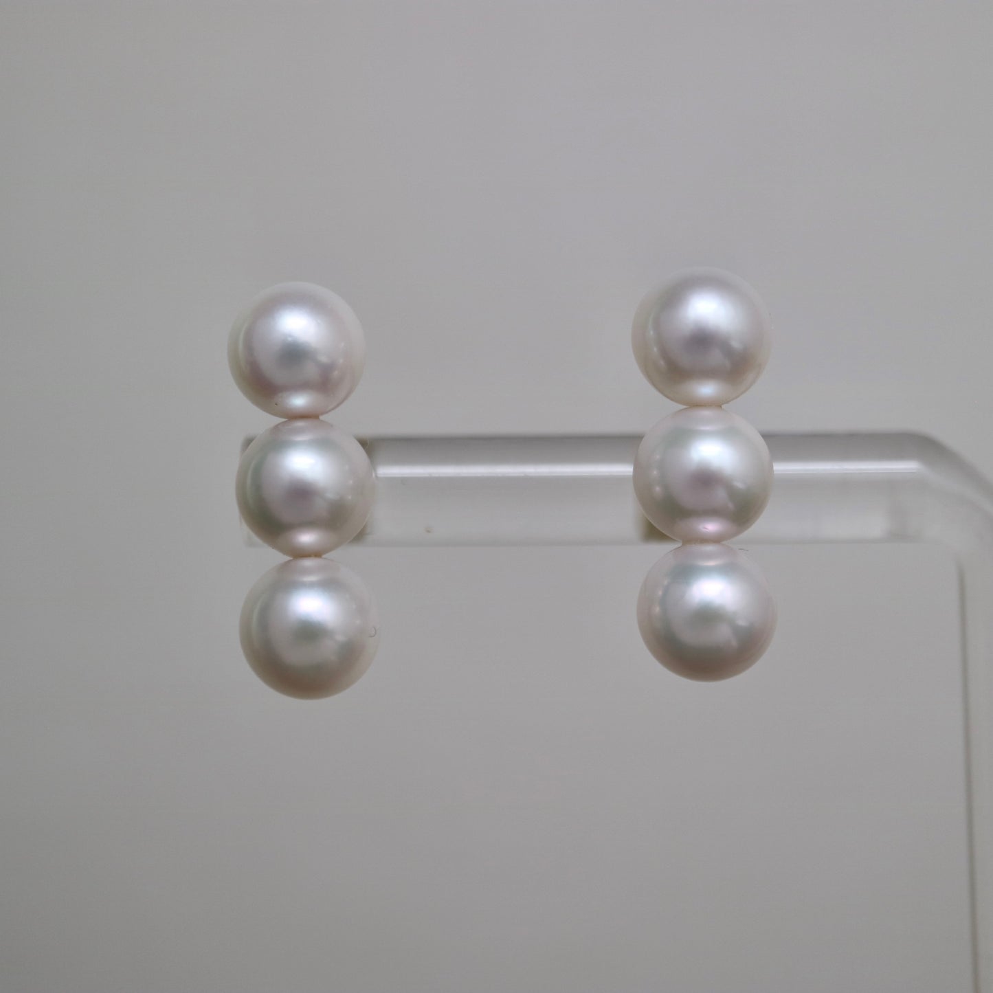 Handmade Japanese Akoya pearl earrings with three lustrous pearls each, displayed on clear stand