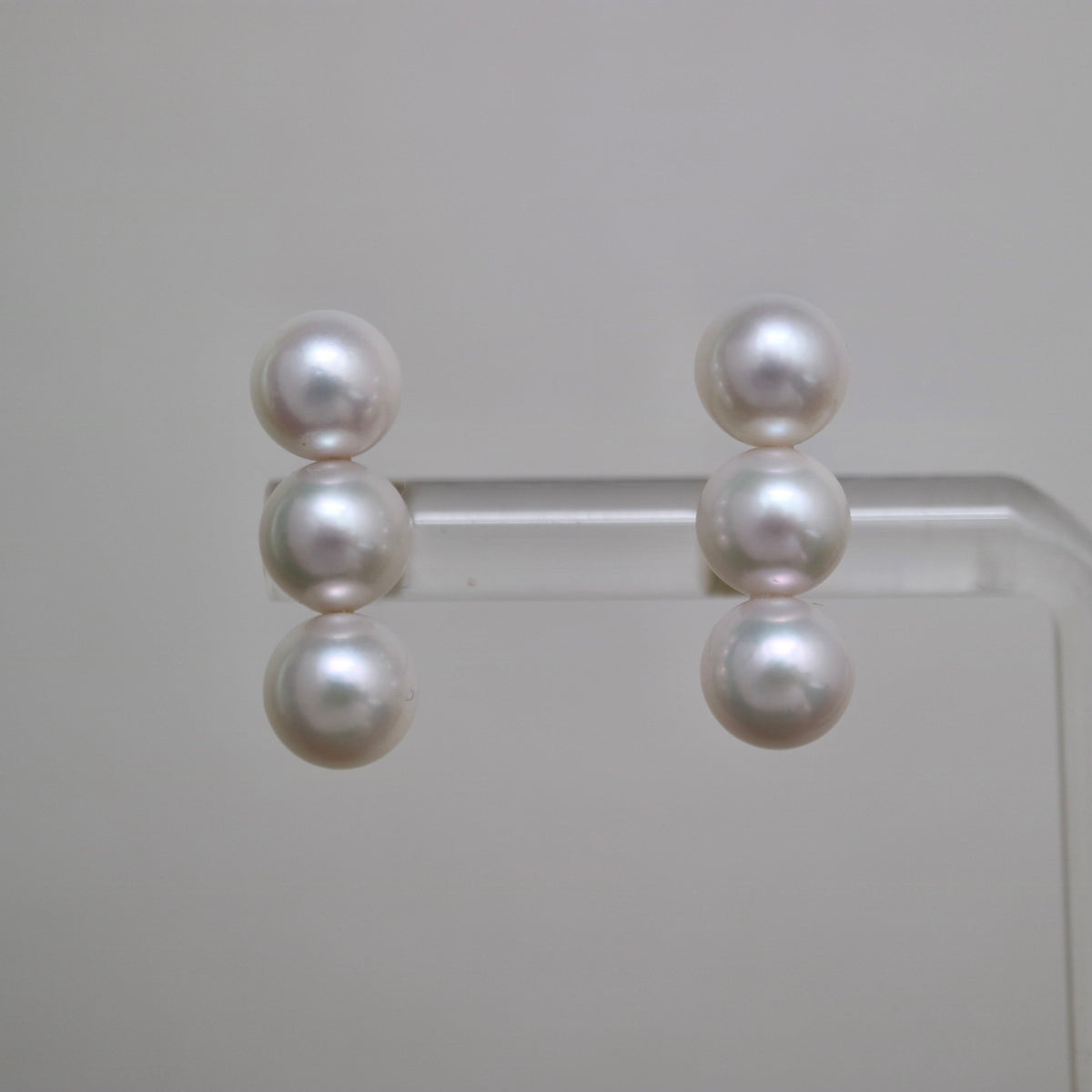 Handmade Japanese Akoya pearl earrings with three lustrous pearls each, displayed on clear stand