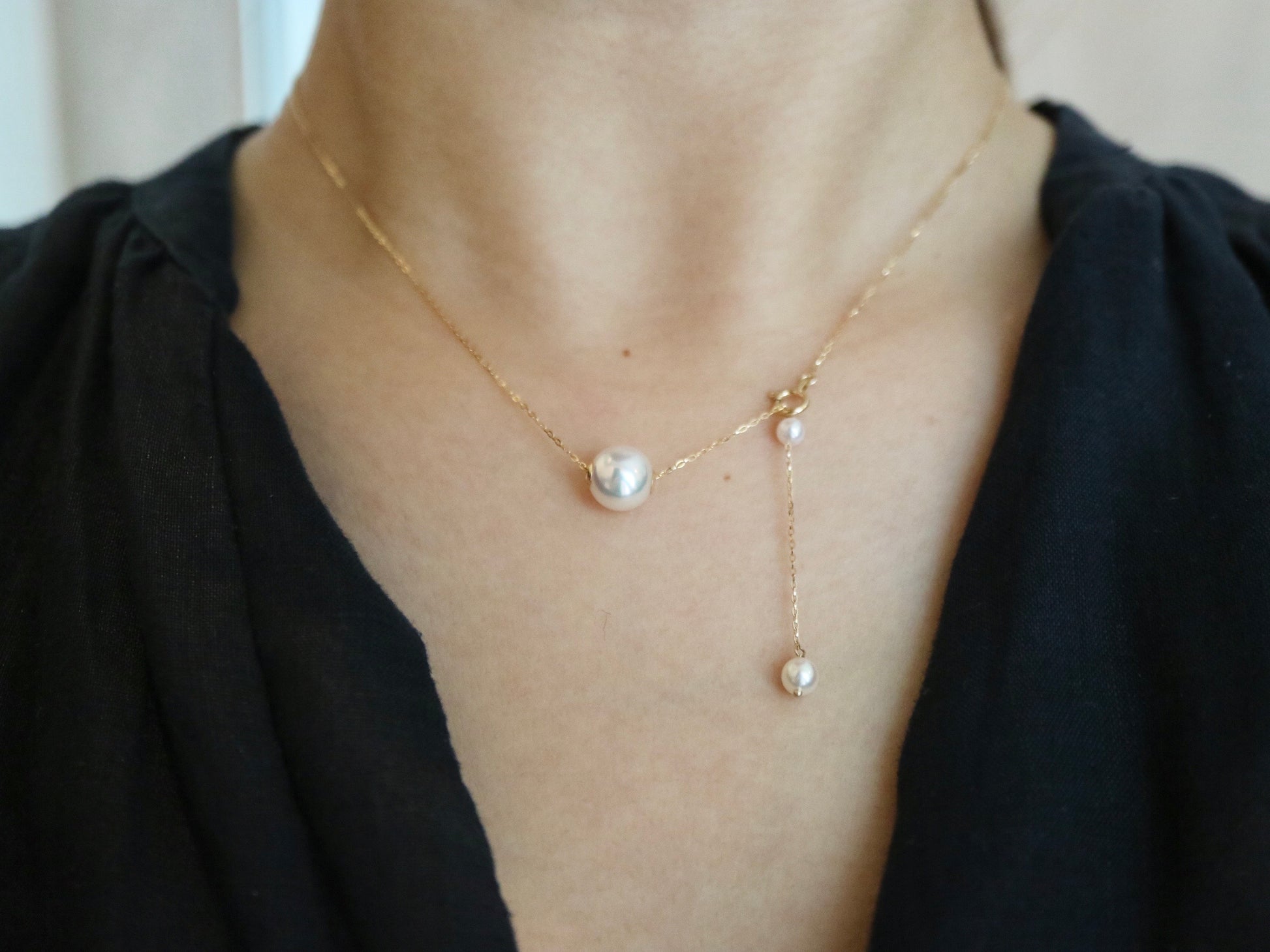 Delicate gold chain necklace with three pearls worn on a woman's neck and black top