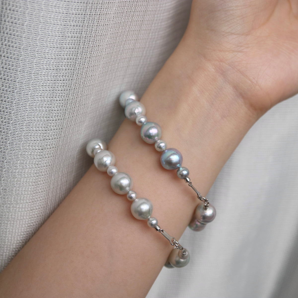 Hand wearing elegant Akoya pearl bracelet with silver-toned clasp, showcasing lustrous seawater pearls on wrist.