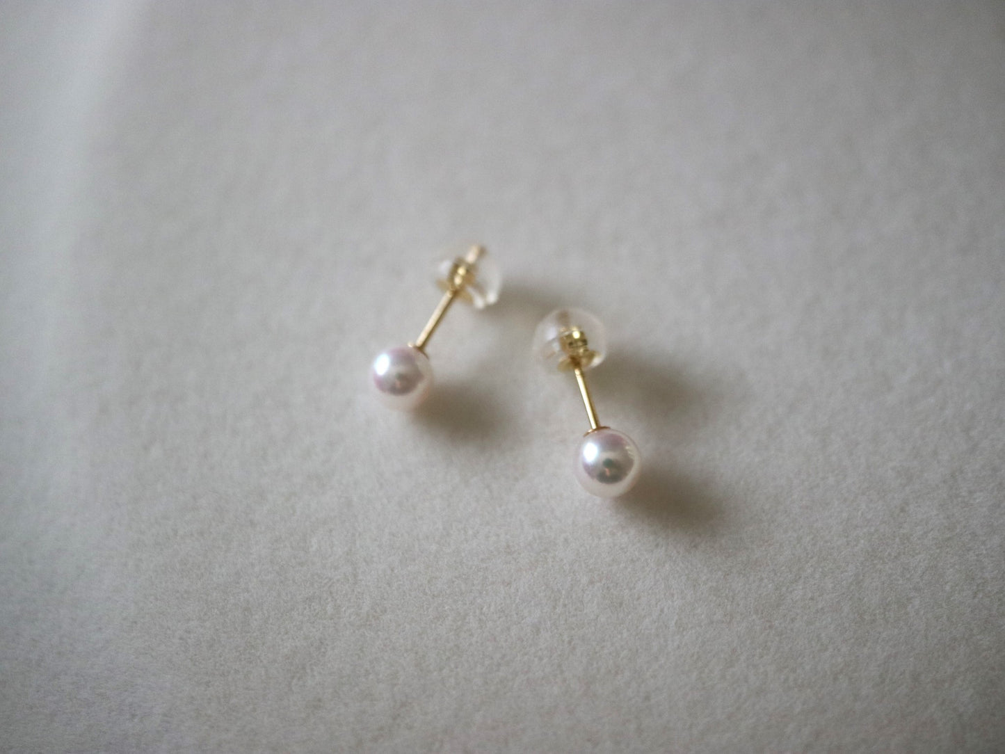 Handmade Akoya pearl stud earrings with gold posts, showcasing lustrous seawater pearls on soft fabric.