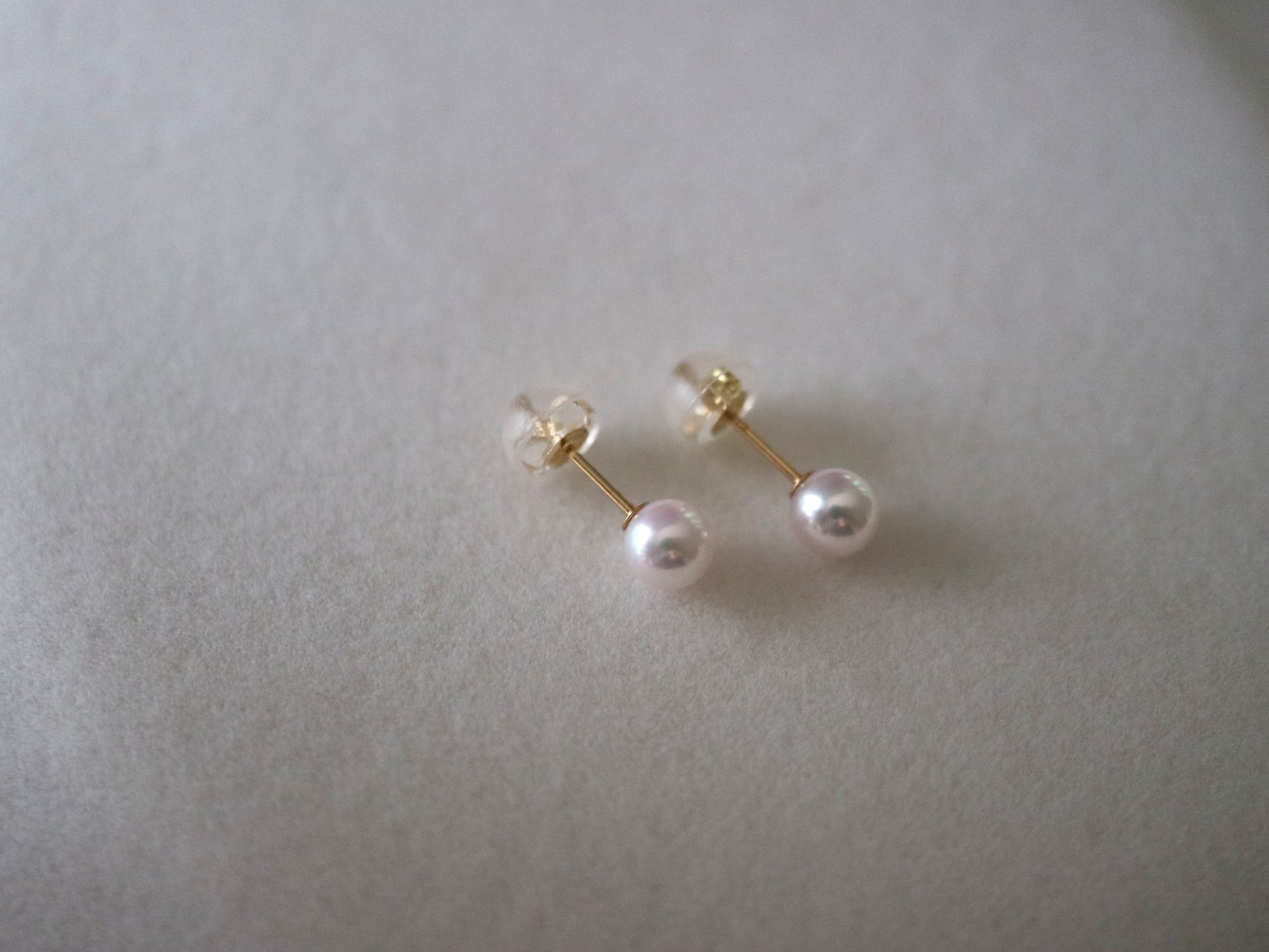 Handmade Japanese Akoya pearl stud earrings with gold posts, showcasing lustrous seawater pearls on soft gray background.