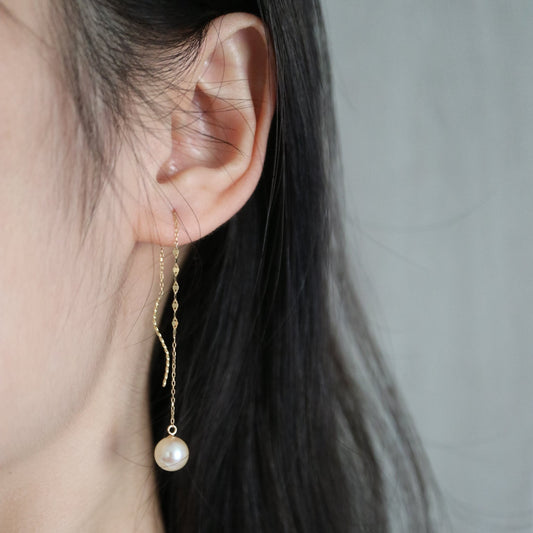 Close-up of an ear wearing a delicate gold chain earring with a single Japanese Akoya pearl pendant