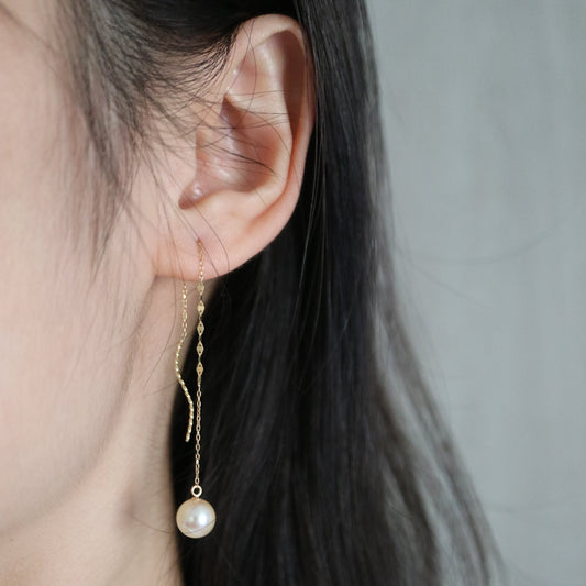 Close-up of an ear wearing a delicate gold chain earring with a single Japanese Akoya pearl pendant