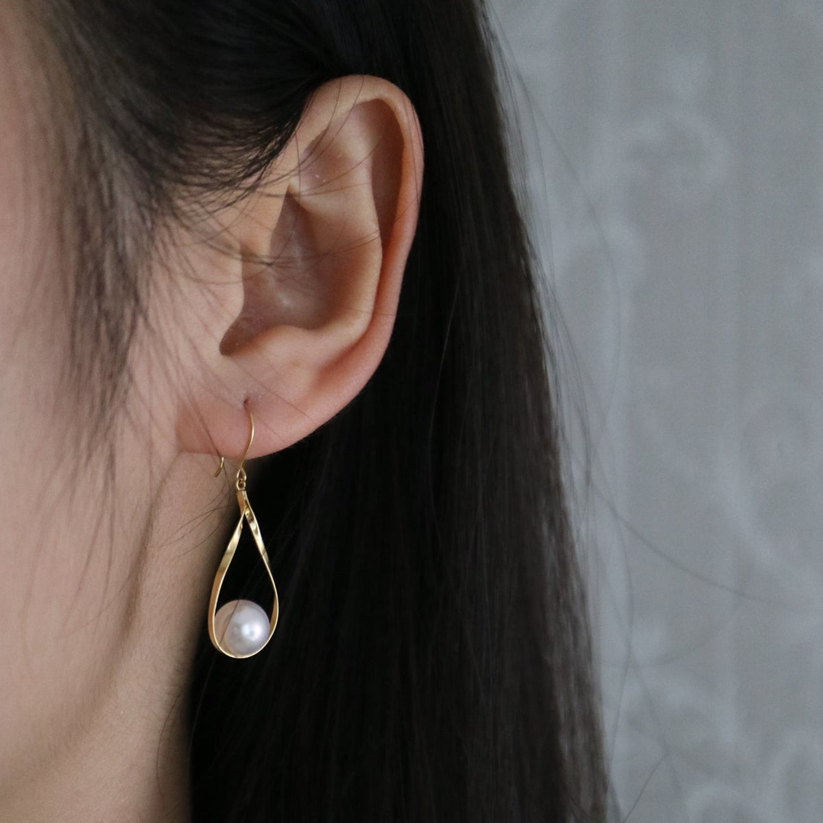 Close-up of a gold teardrop earring with a white Akoya pearl worn on an ear