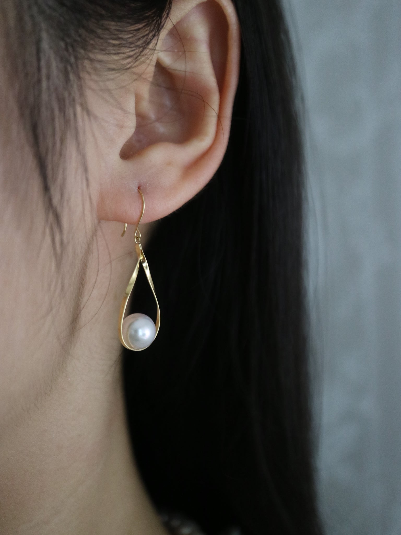 Handmade gold drop earring with a single white Akoya pearl worn on an ear