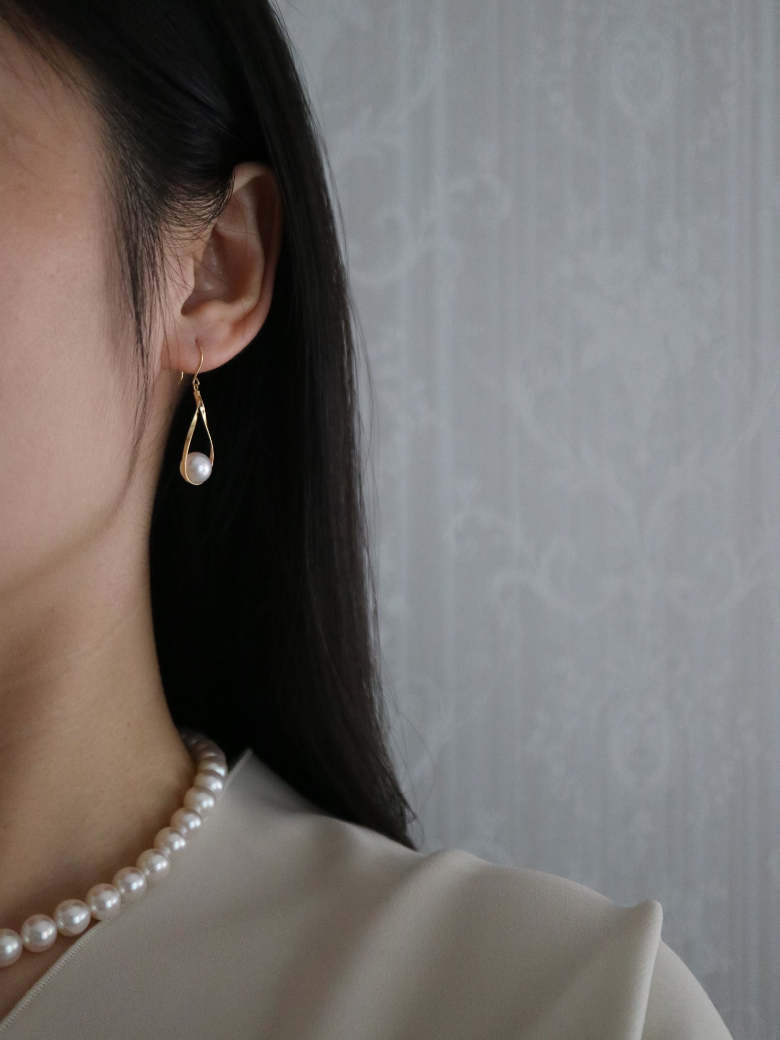 Close-up of a woman wearing a gold teardrop Akoya pearl earring and matching pearl necklace