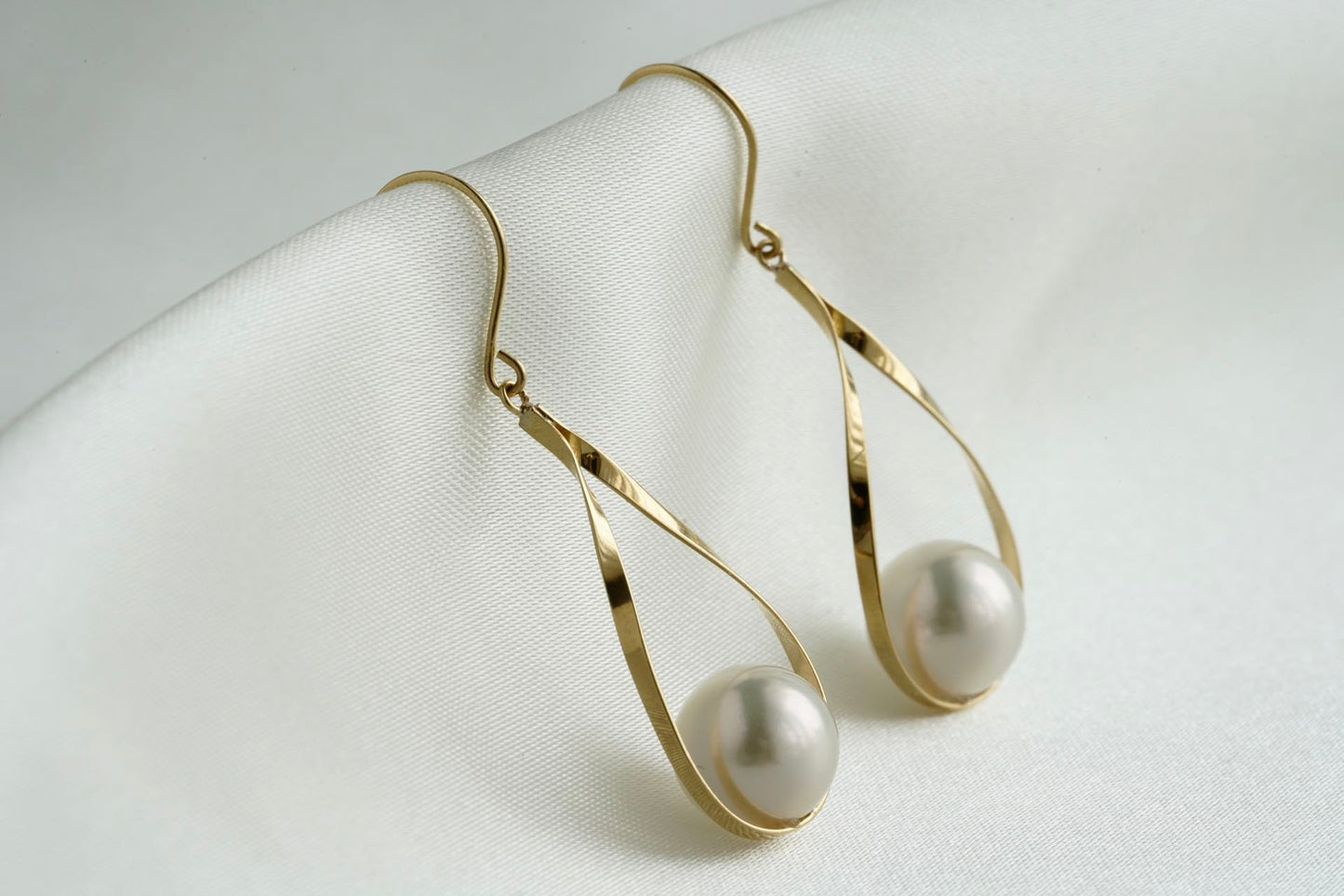 Pair of gold drop earrings with white Akoya pearls on white fabric